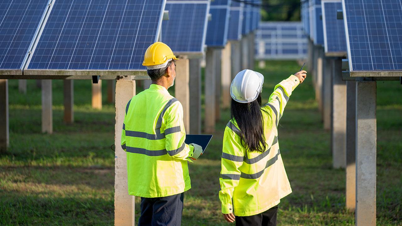 Two engineers in PPE having a discussion in front of a solar array